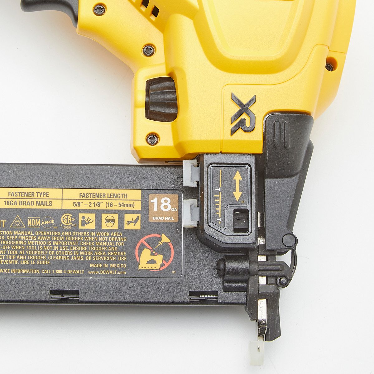 A battery-operated brad nailer sits on a flat surface, ready for use, displaying fastener information and safety warnings alongside its operational parts.