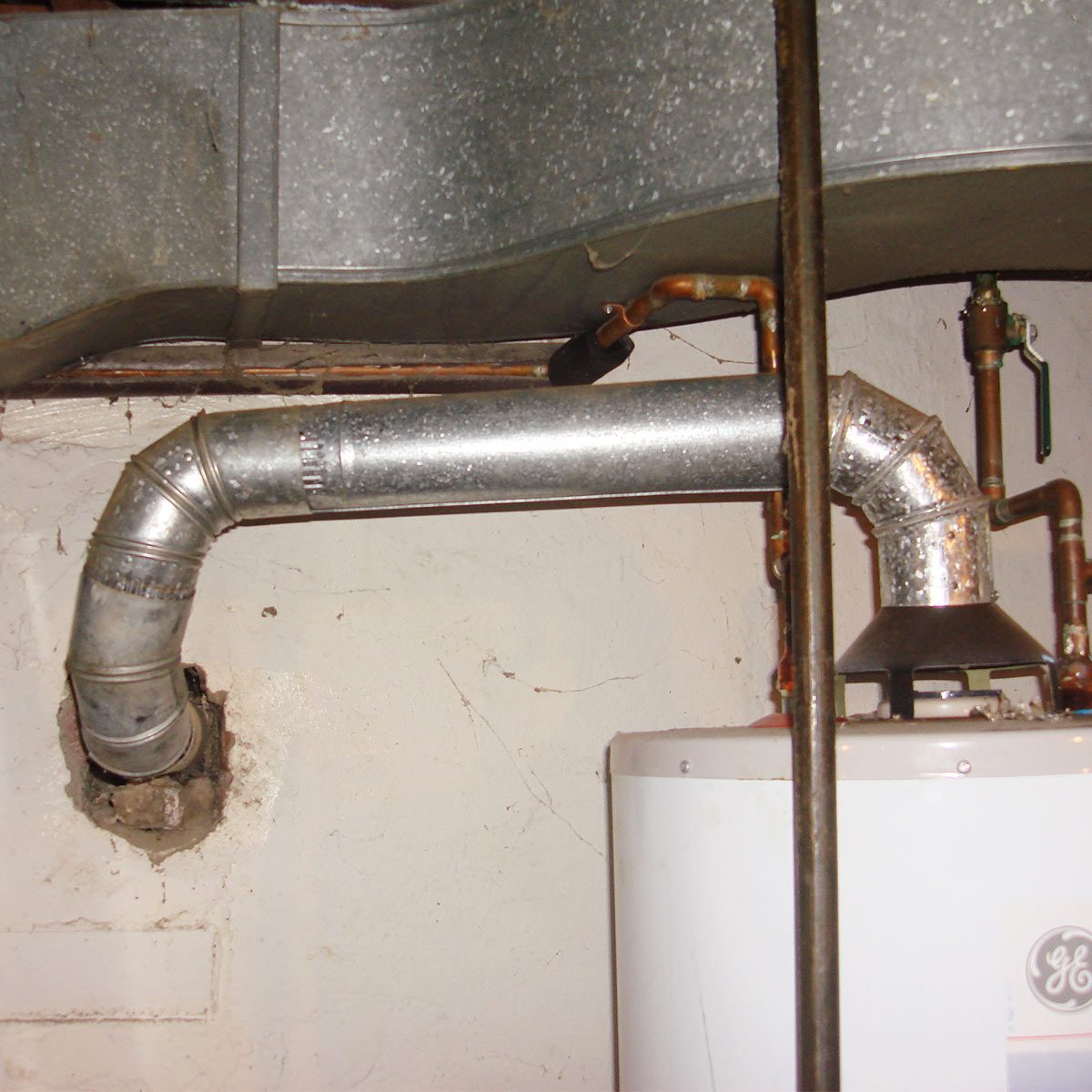 A metallic exhaust pipe connects to a water heater, running along a wall in a basement, with visible plumbing fixtures nearby.