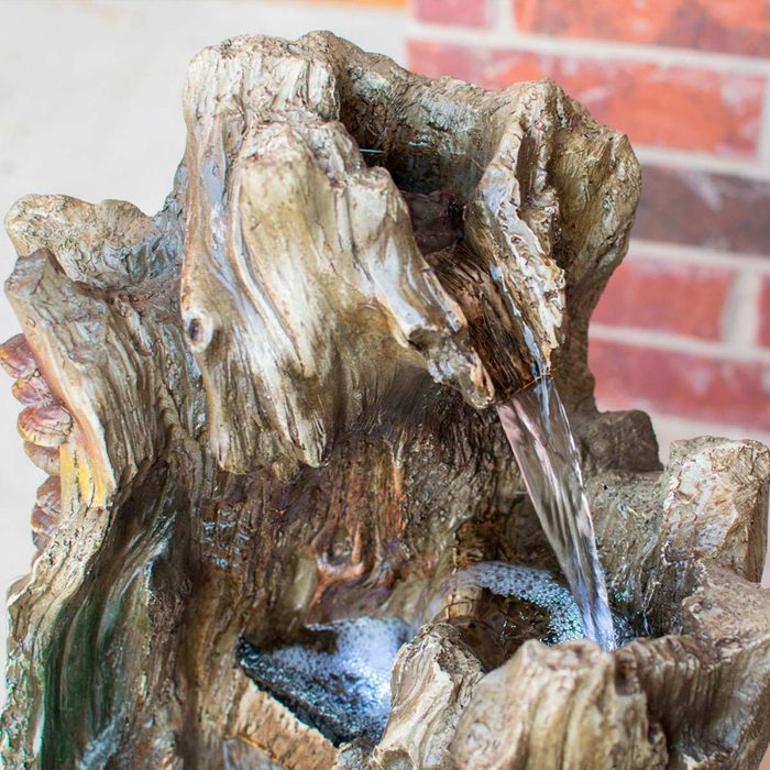 A decorative water fountain, resembling a wooden sculpture, pours water from a crevice, creating a tranquil ambiance against a brick wall backdrop.
