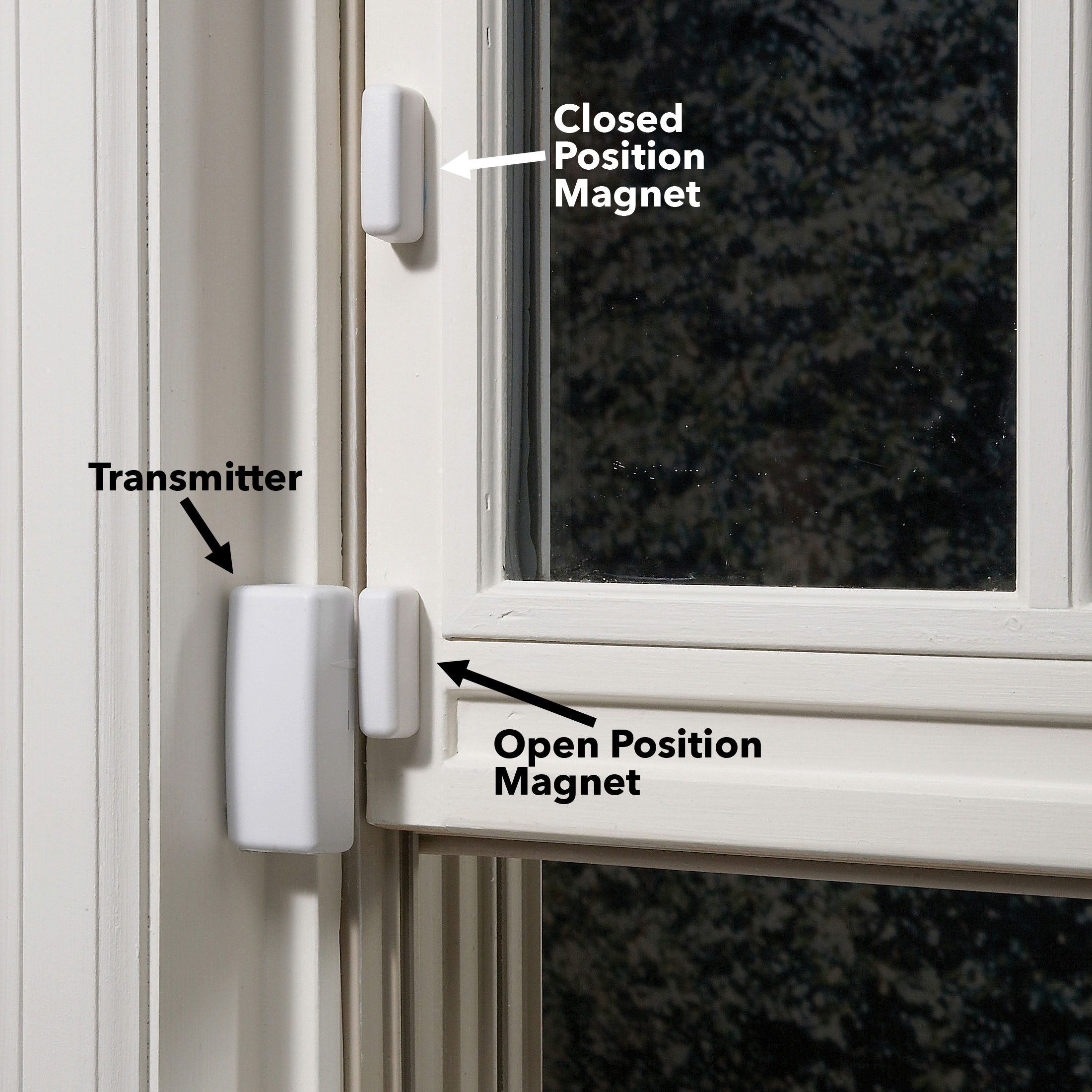 A window has three white magnetic components: a transmitter and two magnets indicating open and closed positions, set against a subtle outdoor background.