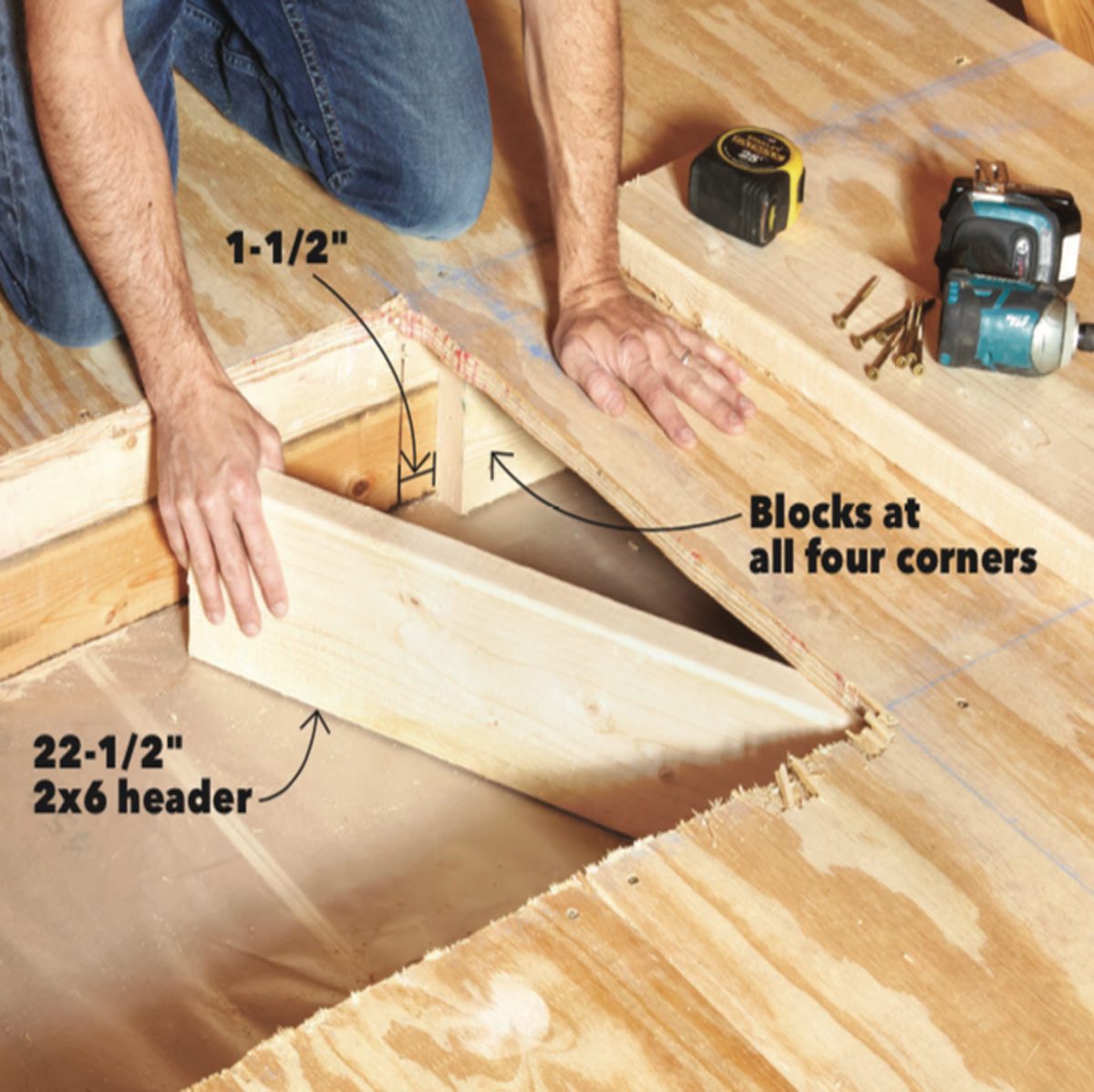 A person places a wooden header into a floor opening while tools and screws are arranged nearby, indicating ongoing construction work.