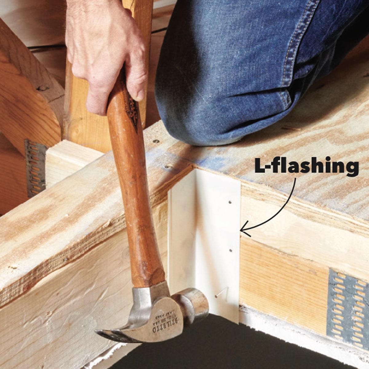 A hammer strikes L-flashing positioned on a wooden beam, with a person kneeling nearby. The setting is a construction area with raw materials visible.