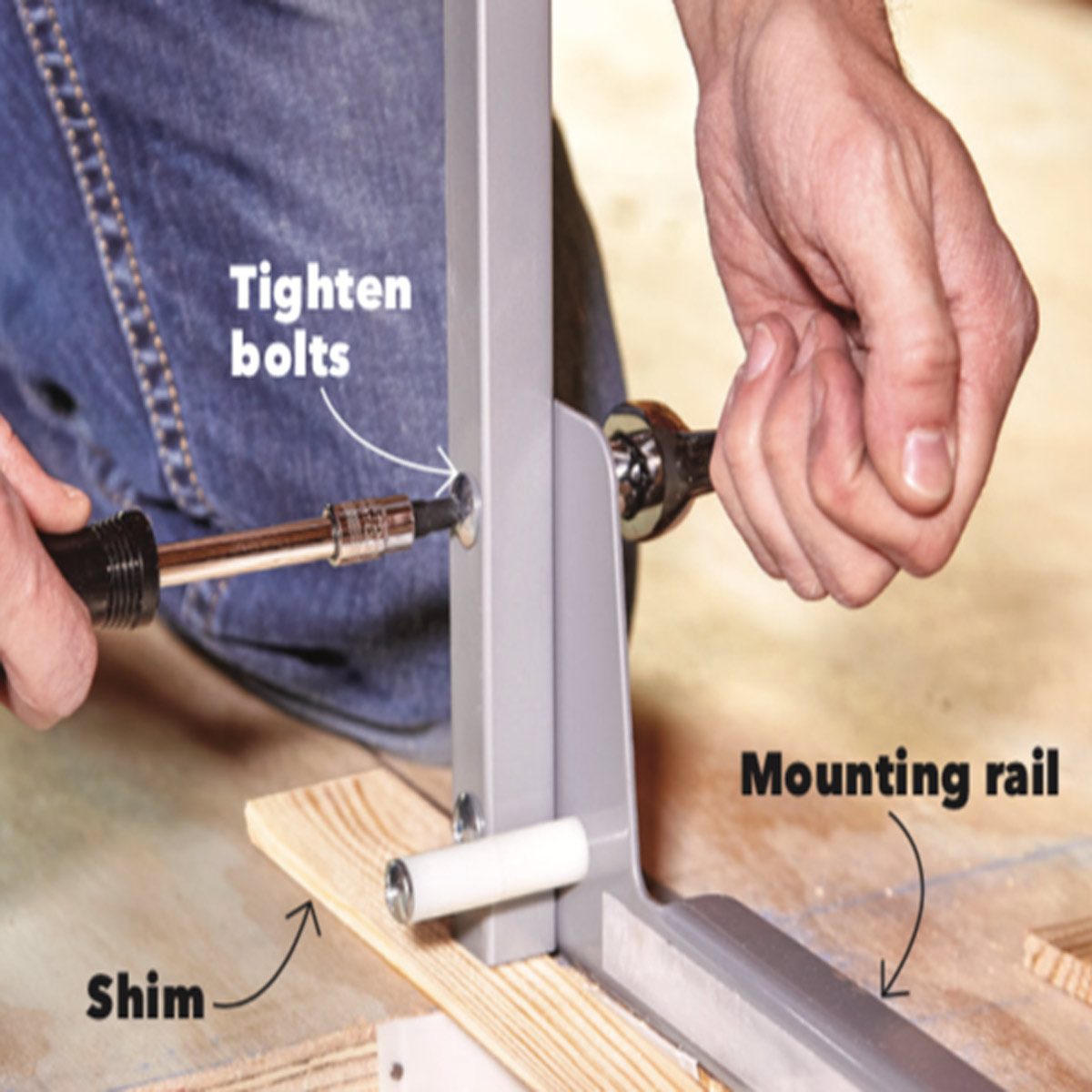 A person tightens bolts on a metal mounting rail, using tools on a wooden surface with a shim beneath it for support.