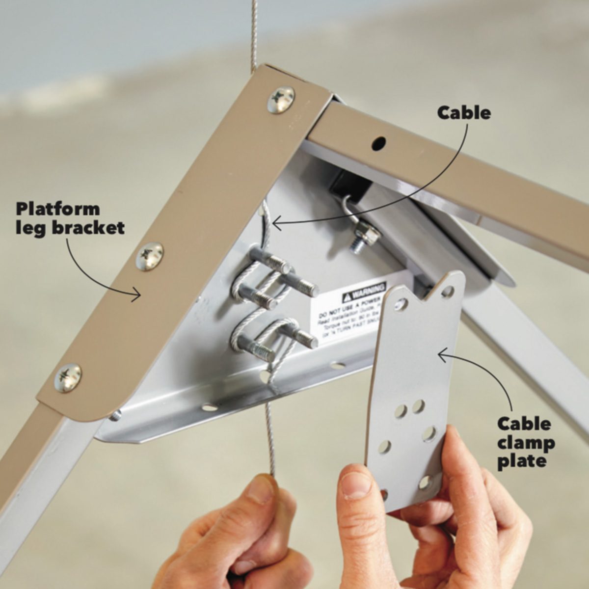 A person holds a cable clamp plate, connecting it to a platform leg bracket, while a cable is integrated into a metal structure in an indoor environment.
