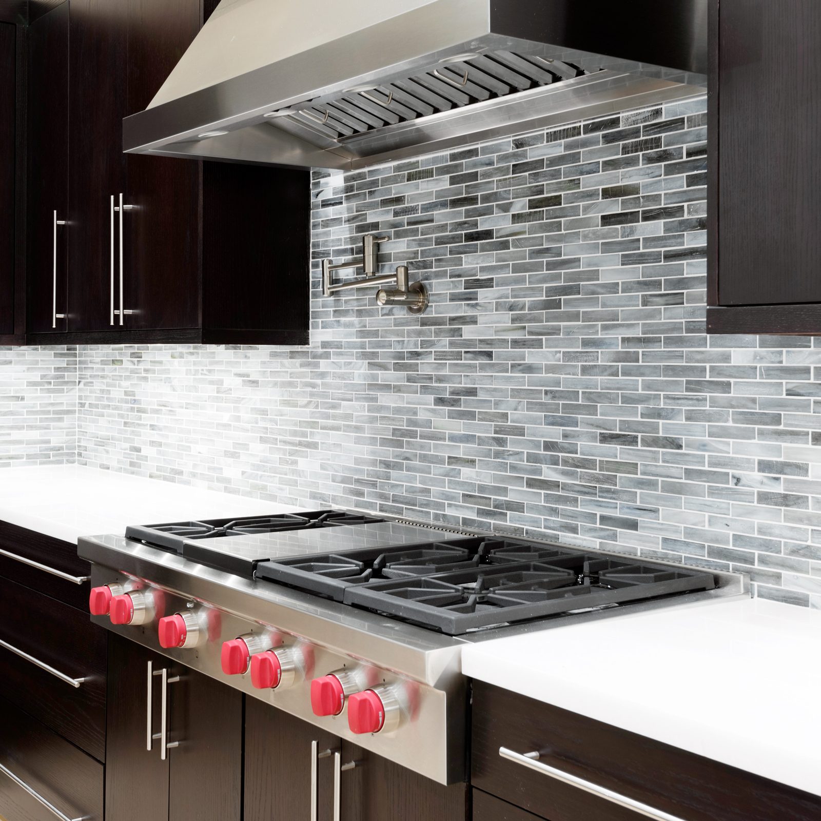 a modern looking kitchen with dark brown cabinets, a white countertop and a grey stone backsplash