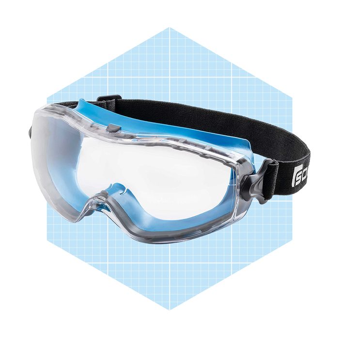 Protective goggles sit tilted with a blue and clear design. They are displayed against a light blue grid pattern background, highlighting their safety features.