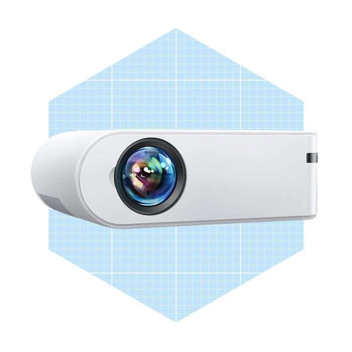 A white projector sits horizontally, showcasing its colorful lens, against a light blue grid-pattern background.