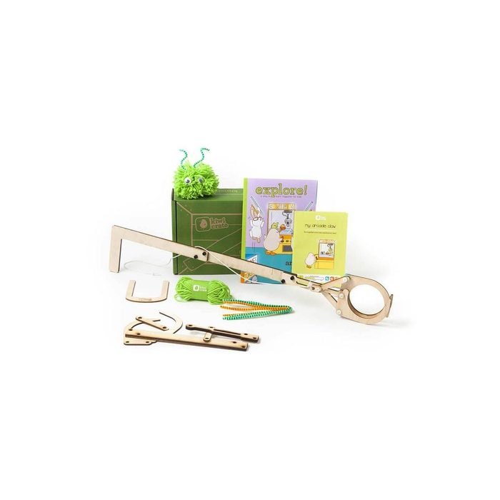 A wooden tool with a circular opening sits beside educational booklets, a green pom-pom creature, colored strings, and craft parts on a white background.