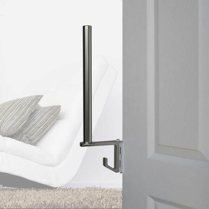 A doorstopper holds a door open, with a vertical pole and hook attachment, against a backdrop of a softly furnished room with a couch and pillows.