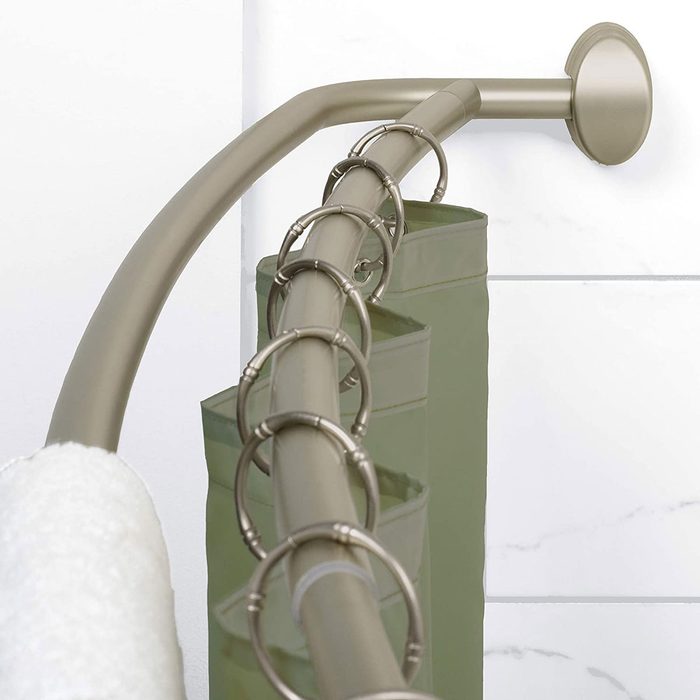 A shower curtain rod holds a green curtain with metal rings, positioned against a light, glossy wall, with a white towel on display nearby.