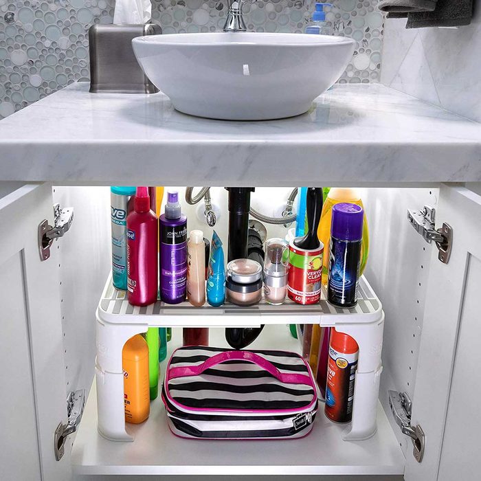 A white sink rests on a marble countertop. Below, a cabinet showcases various personal care products organized on shelves, illuminated softly.