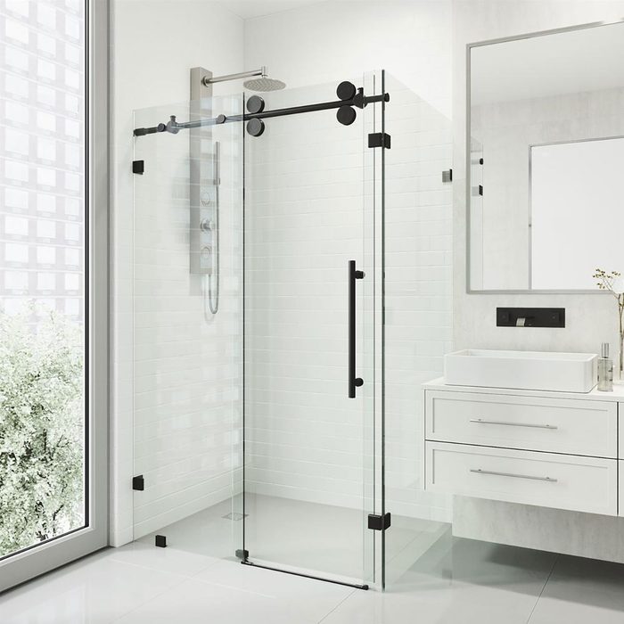 A glass shower enclosure stands with a rainfall showerhead above, set in a modern bathroom featuring white tiles and a sleek vanity with a mirror.