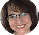 A smiling person with glasses is facing the camera, showcasing a warm expression, set against a neutral background.