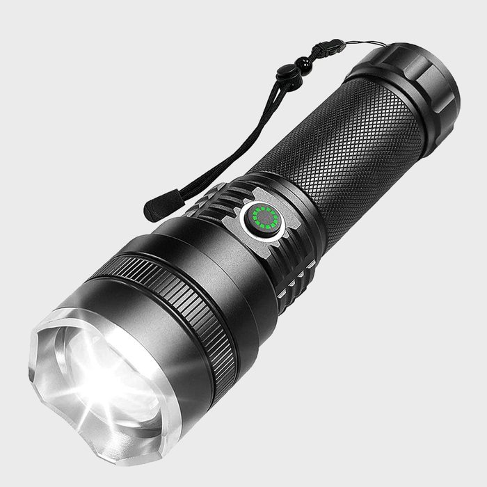 A black flashlight emits bright light, featuring a textured grip and a green indicator. It's positioned against a plain background, ready for use.