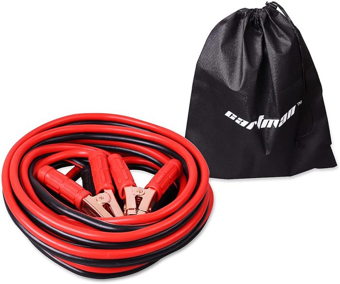 A coiled set of red and black jumper cables with alligator clips rests beside a black drawstring bag, indicating storage for automotive use.