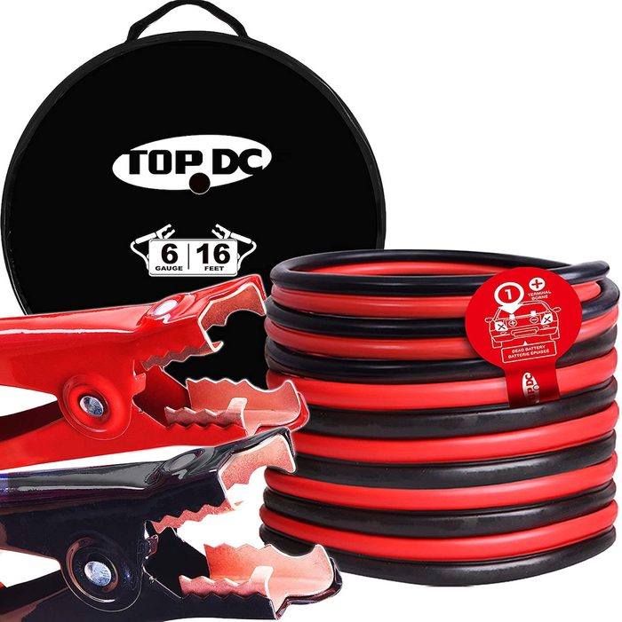 Red and black jumper cables are coiled beside metal clamps, ready for use. A storage case is visible in the background, indicating organized vehicle maintenance tools.
