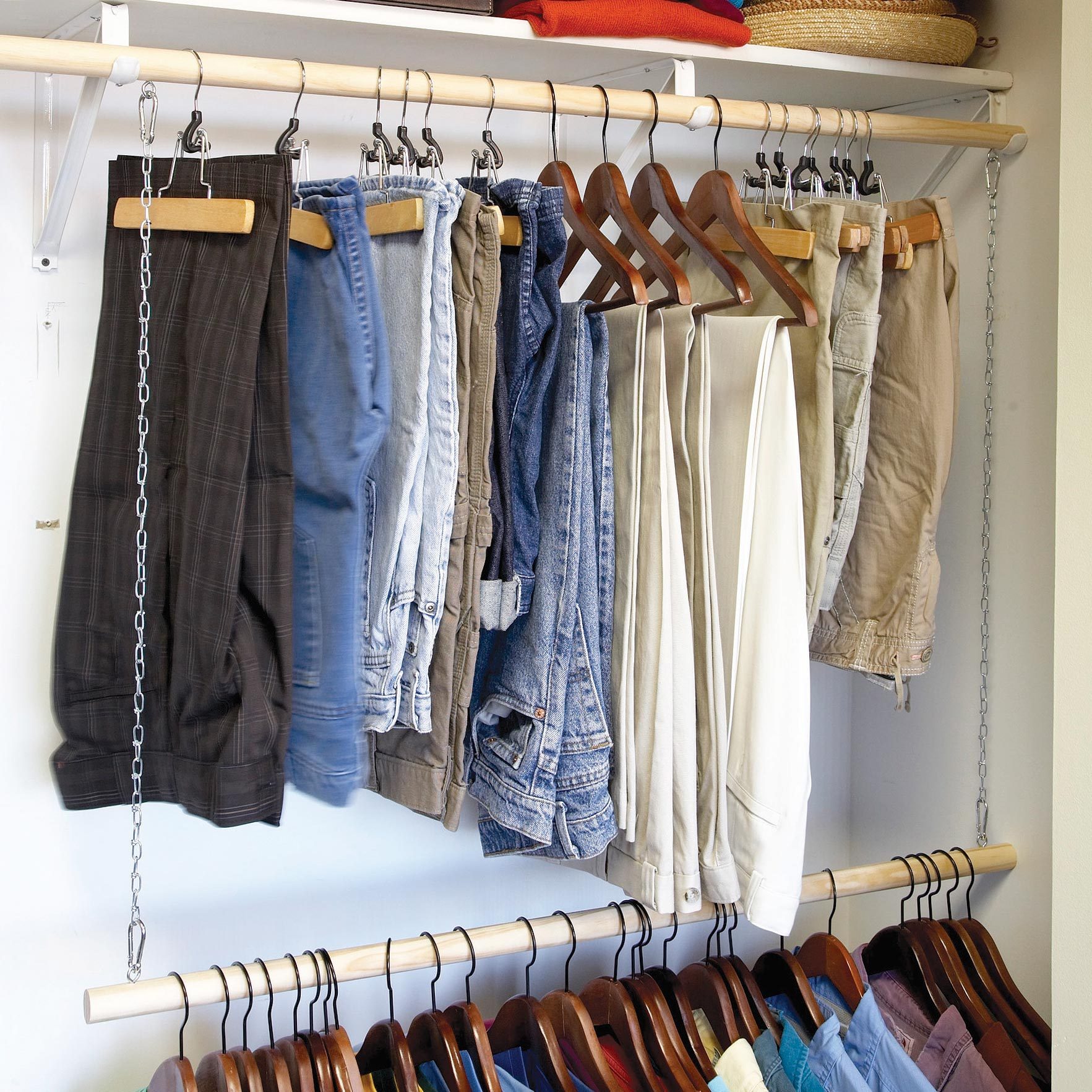 Pants hang from hooks and hangers in a closet, showcasing various colors and styles, with shirts displayed below on wooden hangers.