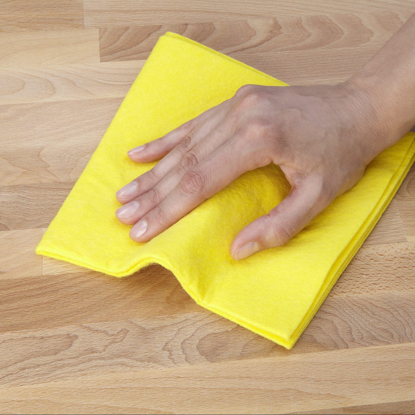 A hand presses a yellow cleaning cloth against a wooden surface, indicating cleaning or wiping action in a tidy indoor environment.
