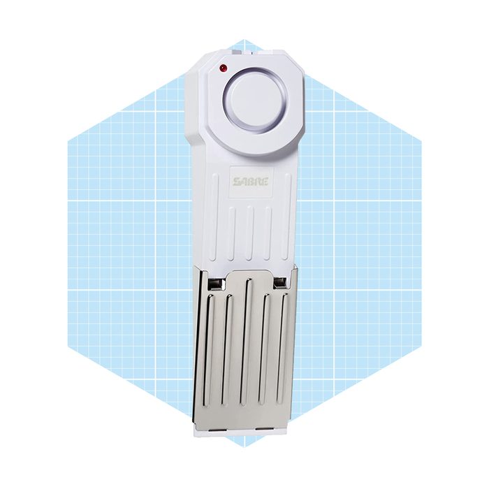 A safety device with a round button and red light is resting against a light blue grid-patterned background, designed to enhance personal security.