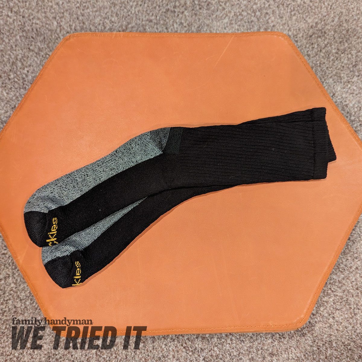 Two pairs of socks, one black and one gray, resting on a brown, hexagonal surface in a textured gray setting.