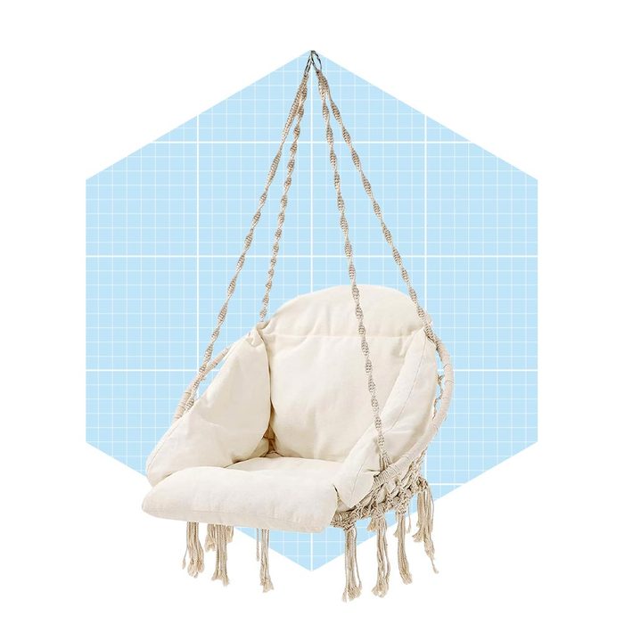 A macramé swing chair hangs from ropes, gently swaying against a light blue grid background, inviting relaxation and comfort.