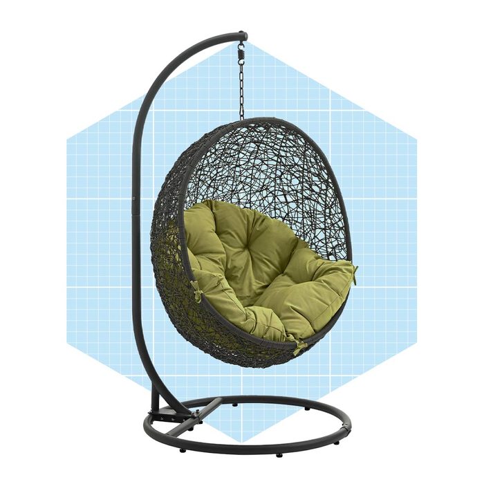 A hanging egg chair with a dark woven exterior and green cushions sways gently, supported by a curved black frame against a light blue grid background.