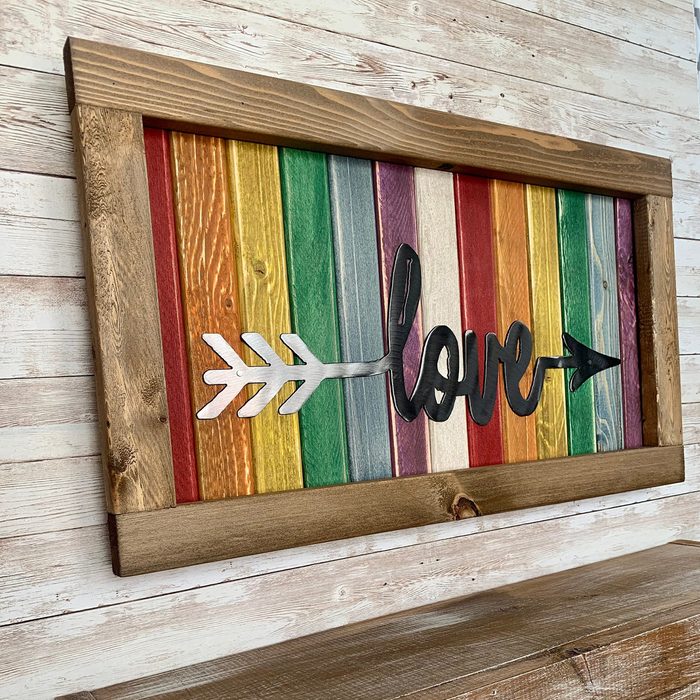 A wooden sign with rainbow-colored vertical slats displays the word 