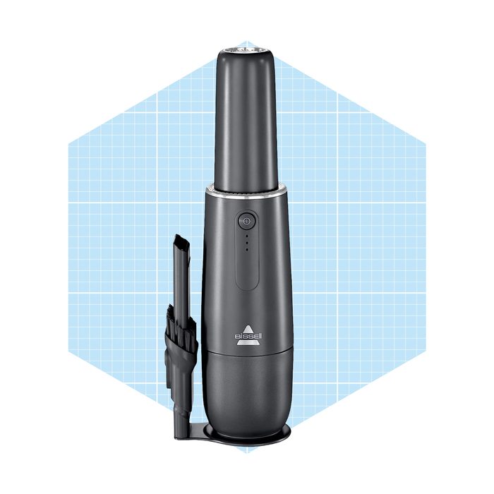 A black handheld vacuum cleaner stands upright. Its nozzle is pointed upward. The background features a light blue grid pattern, suggesting a modern design.
