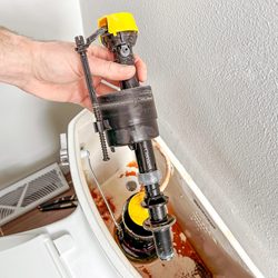 Hand holding Fill Valve over toilet tank